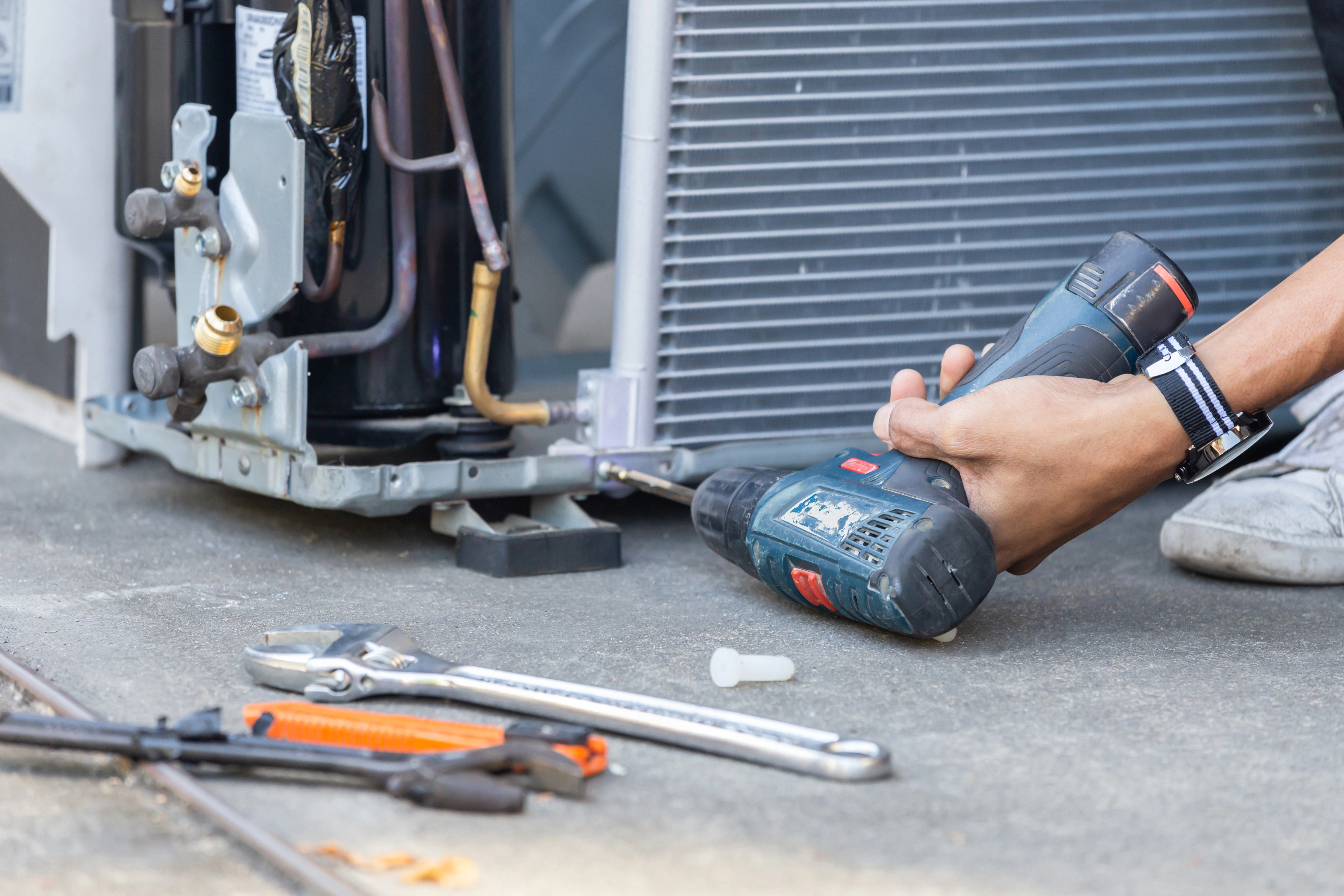 A technician uses a power drill on an AC compressor as part of a repair in Catoosa.