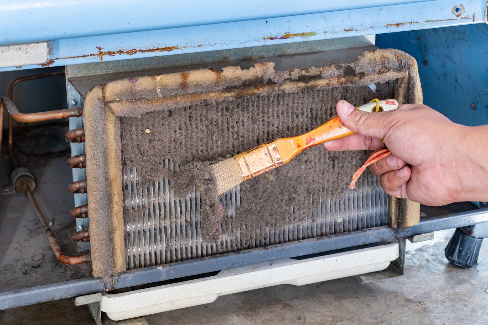 An Air Dynamics of Tulsa technician cleaning a heavily clogged evaporator coil as part of an AC maintenance service in Tulsa, OK.